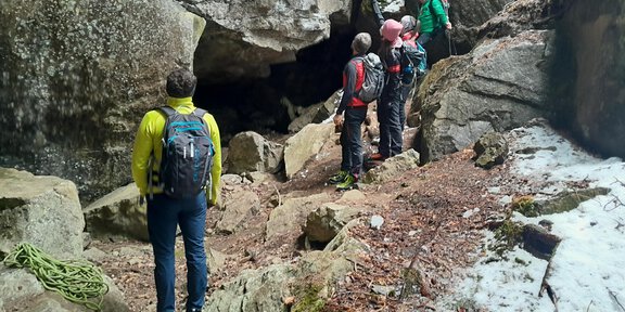 A group of hikers stands in a rocky environment. They are exploring a cave, surrounded by large stones and in a natural landscape. - Abenteuer im Bergsturzlabyrinth – das Geheimnis des Tauferbergs