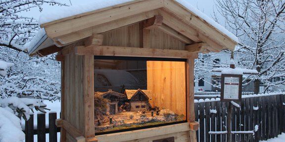 A cozy wooden cottage stands in a snowy landscape. Inside, a small Christmas nativity scene is illuminated. - Andachtsfeier der Sternenkinder | © Patrick Falkner
