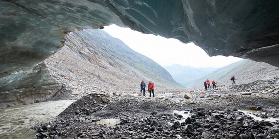 A group of hikers explores a glacier landscape. In the background, there are mountains and a gray sky. - Gletscherspaltentour