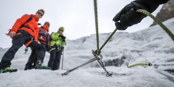 A group of climbers is standing on a glacier. One person is holding a rope while preparing for the ascent. - Gletscherspaltentour