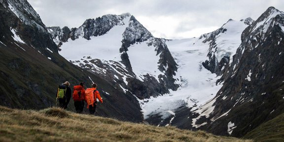 A group of hikers is moving through an alpine landscape with snow-covered peaks. The sky is cloudy, and nature displays an impressive beauty. - Gletscherspaltentour