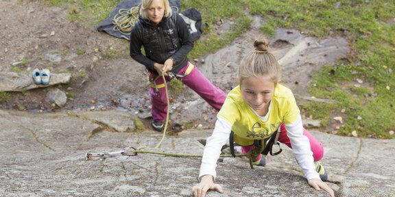 Two girls rock climbing. One is ascending the wall while the other is securing her. - Klettersteig Workshop