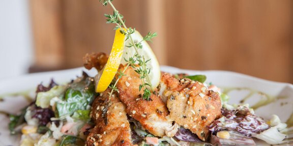 A plate with crispy fish, garnished with fresh lemon juice and thyme. Underneath lies a colorful salad. - Sonnblick - Hochsölden