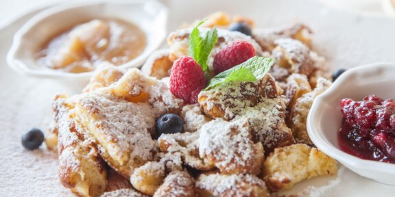 A delicious dish with sliced, sugar-sprinkled dough pieces, garnished with raspberries and mint. Served with applesauce and fruit jam. - Sonnblick - Hochsölden