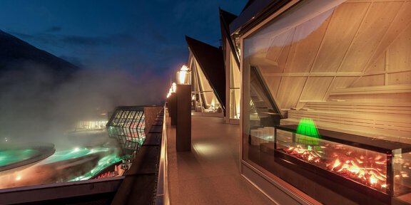 A modern spa with elegant architecture and a warm atmosphere. Outside, a steaming thermal bath is visible at night. - Aqua Dome "Treatment & Spa" - Längenfeld