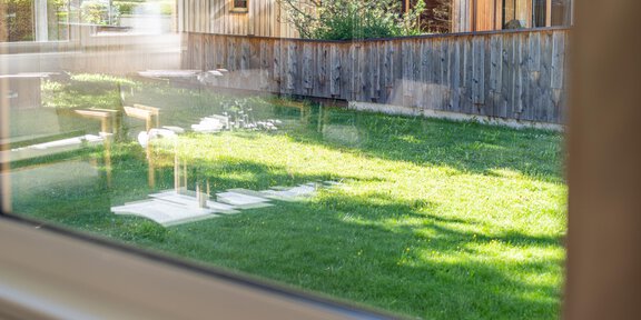 A well-maintained lawn in front of a wooden house with a wooden fence. In the background, trees and a sunny sky can be seen. - Konferenzraum Hotel Falknerhof am Ursprung - Niederthai | © Hotel Falknerhof