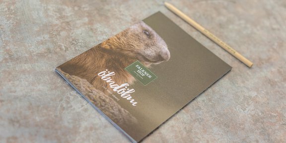 A notebook with an image of a marmot on the cover is lying on a tabletop. Next to the notebook is a pencil. - Konferenzraum Hotel Falknerhof am Ursprung - Niederthai | © Hotel Falknerhof