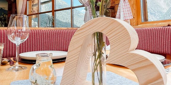 Ein gemütlicher Tisch in einem Holzhaus, dekoriert mit einem herzförmigen Holzvase und Blumen. Große Fenster bieten einen Blick auf die Berge und die natürliche Umgebung. - Bergzauber - Sölden