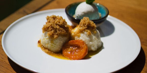 A plate with two filled dumplings, topped with crumbs. Next to it is a small bowl with ice cream and a caramelized fruit. - Grüners Wirtshaus - Sölden