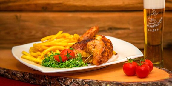 Ein Teller mit knusprigem Hühnchen, Pommes frites und frischen Tomaten. Dazu ein Glas Bier auf einem Holzbrett. - Hühnersteign - Sölden