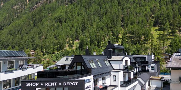 A modern sports store in a mountain village, surrounded by green mountains. The sky is clear and there is plenty of daylight. - Sport4You Filiale Giggijoch - Sölden