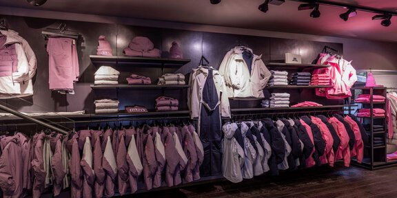 Ein Verkaufsregal mit verschiedenen Bekleidungsstücken in Pink- und Lilatönen. Die Kleidung ist ordentlich angeordnet und umfasst Jacken und Sweatshirts. - THE MOUNTAIN STUDIO - Sölden