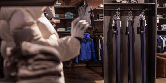 Ein moderner Bekleidungsladen mit verschiedenen Sportbekleidungsstücken und Accessoires. Links ist eine Winterjacke zu sehen, während rechts mehrere Gürtel ausgestellt sind. - THE MOUNTAIN STUDIO - Sölden