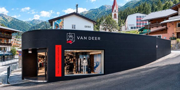 Ein modernes Geschäft mit schwarzer Fassade, das die Marke "VAN DEER" präsentiert. Im Hintergrund sind alpine Berge und typische Gebäude zu sehen. - THE MOUNTAIN STUDIO - Sölden