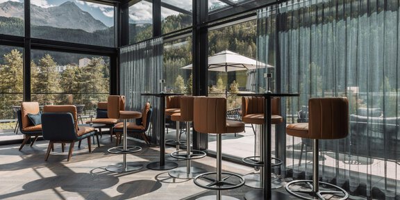 A modern café with large windows and a view of the mountains. The decor is stylish with high tables and chairs. - THE VUE Skybar - Sölden