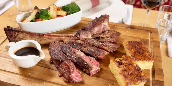 Ein köstliches Fleischgericht auf einem Holzbrett, begleitet von einer Sauce und Beilage aus Gemüse und Brot. Der Tisch ist elegant gedeckt mit Gläsern und Besteck. - Wirtshaus am Giggijoch - Sölden
