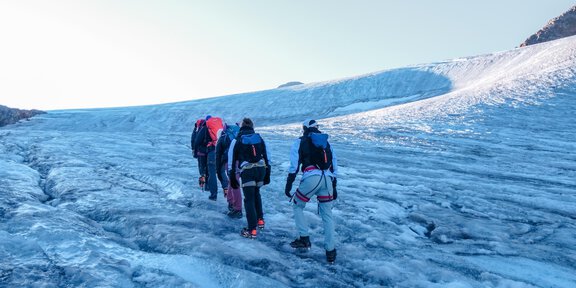 A group of hikers is crossing a glacier. The surroundings are cold and icy, with a clear sky in the background. - Bergführer Vent-Alpin - Vent