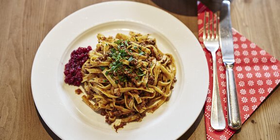 A plate of freshly prepared tagliatelle, garnished with herbs and a side of red berries. Next to it are cutlery and a served tablecloth. - Schöne Aussicht (Hütte) - Vent