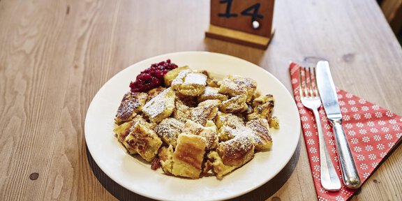 A plate of freshly prepared Kaiserschmarrn, garnished with powdered sugar and cranberries. In the background, there is a table stand with the number 14. - Schöne Aussicht (Hütte) - Vent