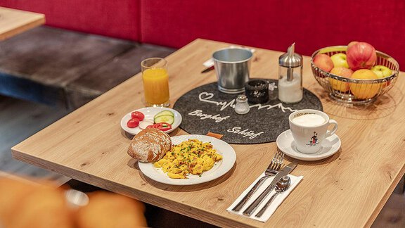 A breakfast table with scrambled eggs, fresh rolls, and a fruit basket. There is also coffee and an orange juice. - Berghof Schöpf - Gries