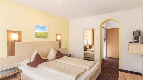 A cozy hotel room with a double bed and modern design. Pictures hang on the walls, and there is a large window that lets in natural light. - Berghof Schöpf - Gries