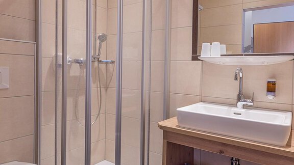 A modern bathroom with a shower cubicle and a sink. The walls are brightly tiled, and there are blue towels. - Berghof Schöpf - Gries