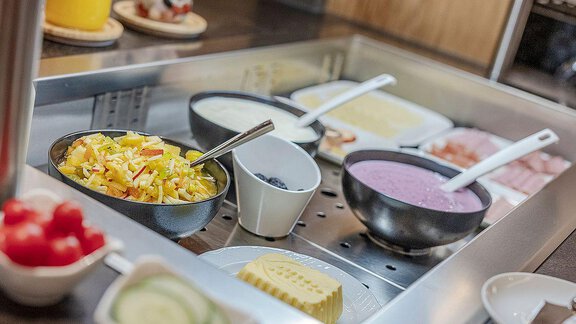 A breakfast buffet with various bowls full of salads, yogurt, and cheese. Fresh ingredients like cucumbers and tomatoes are also available. - Berghof Schöpf - Gries