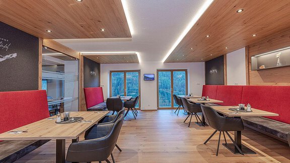 A modern restaurant with wooden decor and red benches. The tables are elegantly set, and large windows offer a view of nature. - Berghof Schöpf - Gries