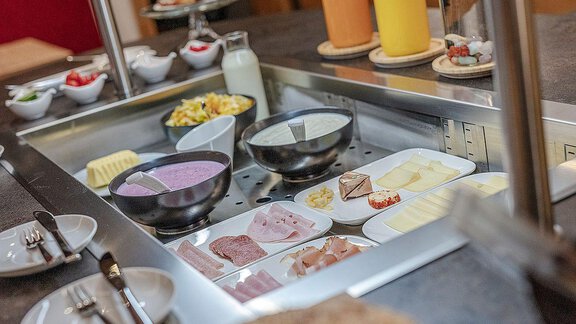 A hearty breakfast buffet with various types of cheese, cold cuts, and fresh fruit. Additionally, there is yogurt, milk, and fresh juice to drink. - Berghof Schöpf - Gries