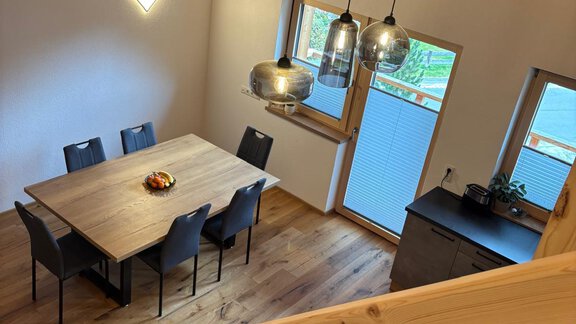 A modern dining area with a large wooden table and six chairs. The room has a bright atmosphere due to large windows and wooden ceilings. - KLAMMERHOF - Gries