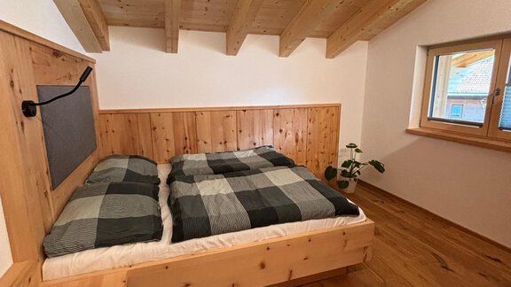 A cozy bedroom with a large, comfortable bed and wooden walls. The room has large windows that let in plenty of daylight. - KLAMMERHOF - Gries