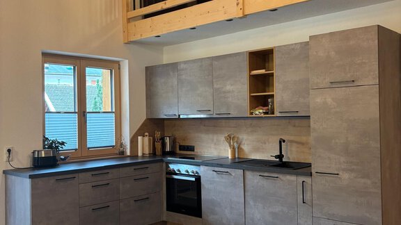 Modern kitchen with wooden furniture and a large window area. The room is bright and friendly, with an open ceiling and a gallery above. - KLAMMERHOF - Gries