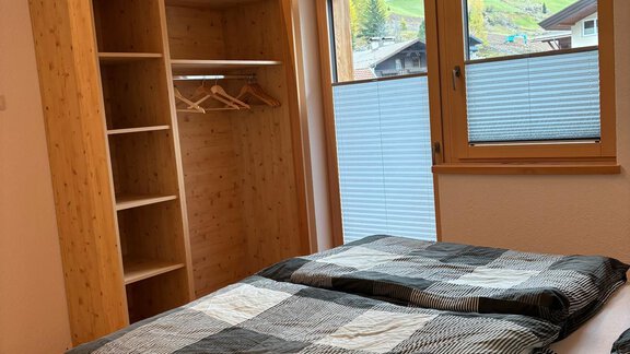 A cozy bedroom with two beds and a wooden shelf. Large windows offer a view of the surrounding nature. - KLAMMERHOF - Gries