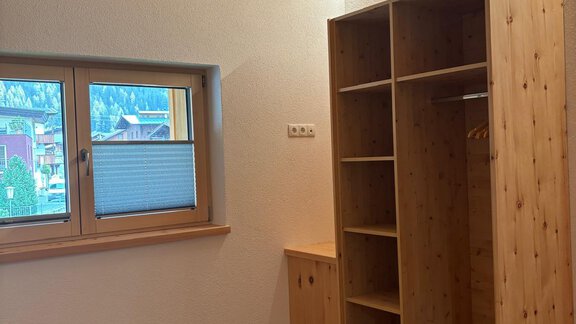 A cozy bedroom with wooden details and a large window.  
The room has a bed with checkered bedding and an open wardrobe. - KLAMMERHOF - Gries