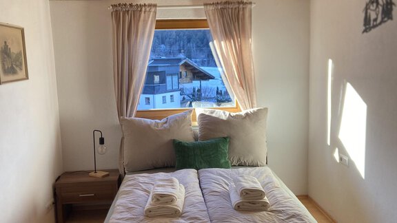Ein gemütliches Schlafzimmer mit einem Doppelbett und einem Fenster, das auf eine schöne Aussicht zeigt. Der Raum hat helle Wände und Holzdecke, was eine warme Atmosphäre schafft. - Krumm & Schief Appartments - Haiming