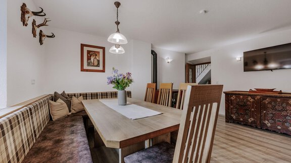 A cozy dining area with a large wooden table and wooden chairs. Decorative elements hang on the walls, and a beautiful bouquet of flowers stands in the center. - Landhaus Waldesruh - Haiming
