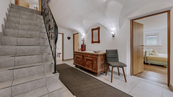 An inviting entrance area with a staircase and a wooden cabinet. To the right, a door leads into another room. - Landhaus Waldesruh - Haiming