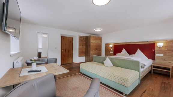A modern room with a large bed and bright walls. There is a table, chairs, and a television that create a cozy atmosphere. - Landhaus Waldesruh - Haiming