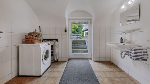 A bright utility room with a washing machine and a sink. The door leads to an outdoor stairway and the room is friendly and inviting. - Landhaus Waldesruh - Haiming