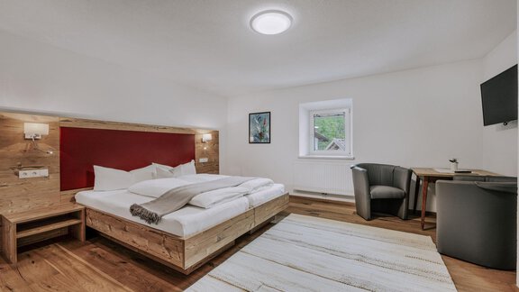 A modern bedroom with a double bed and wooden furniture. A desk and a television complement the cozy decor. - Landhaus Waldesruh - Haiming