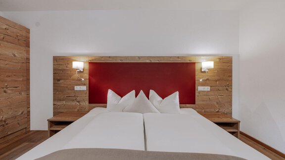 A modern bedroom with a double bed and wooden details. The walls are plain and in light colors. - Landhaus Waldesruh - Haiming
