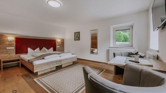 A modern bedroom with a double bed and wooden floor. There is a desk and a window that lets in a lot of light. - Landhaus Waldesruh - Haiming