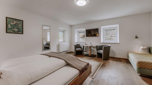 A cozy room with two beds, a table, and armchairs. Bright walls and plenty of natural light create an inviting atmosphere. - Landhaus Waldesruh - Haiming