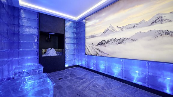 A modern room with walls made of ice blocks and blue lighting. On the wall hangs a large picture of snow-covered mountains. - Alpenhotel Laurin - Hochgurgl