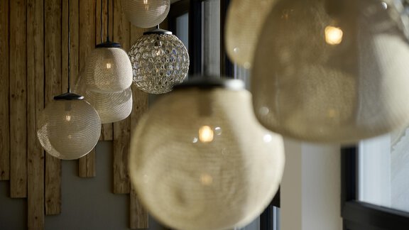 An elegant arrangement of transparent lampshades hangs on a wall. The lighting creates a warm and inviting atmosphere. - Alpenhotel Laurin - Hochgurgl