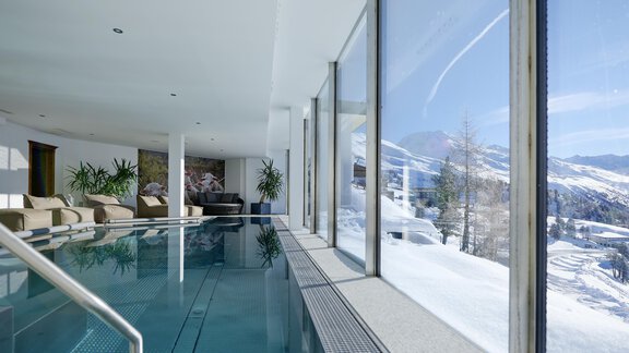 A modern indoor pool with large windows offering a view of snow-covered mountains. The space is bright and inviting, with plants and comfortable seating. - Alpenhotel Laurin - Hochgurgl