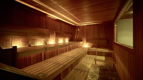 A cozy wooden sauna with warm light. The benches are made of wood and invite you to relax. - Alpenhotel Laurin - Hochgurgl