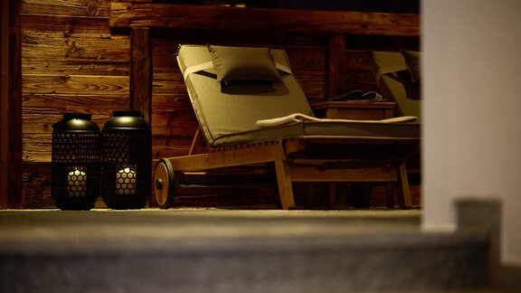 A cozy lounge chair stands next to two decorative lanterns. The wooden paneling in the background creates a warm atmosphere. - Alpenhotel Laurin - Hochgurgl