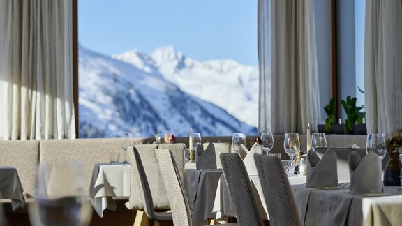 An elegant restaurant with tables and glasses, overlooking snow-capped mountains. The windows let in plenty of light and offer a picturesque view. - Alpenhotel Laurin - Hochgurgl