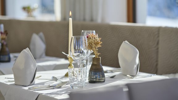 An elegantly set table in a restaurant. The table is decorated with a candle holder, glasses, and a small flower vase. - Alpenhotel Laurin - Hochgurgl